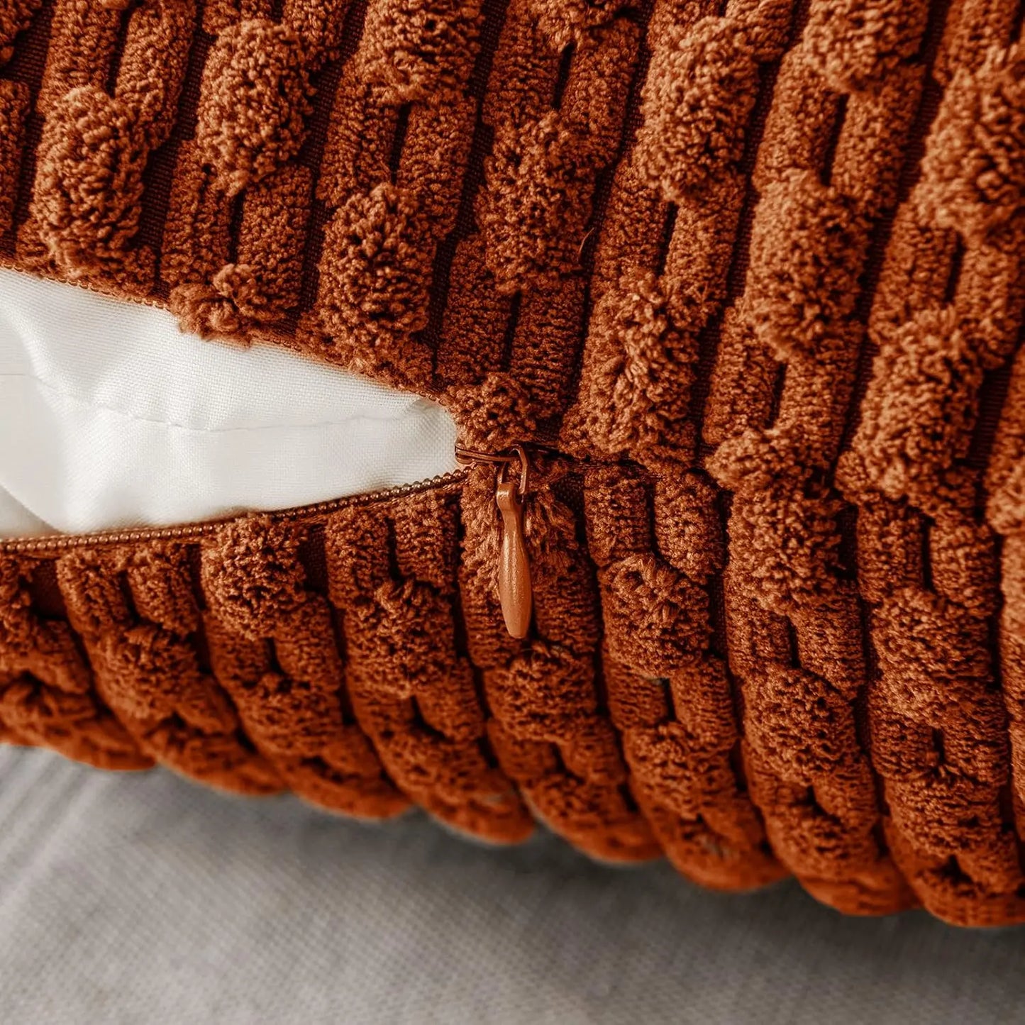 Gros plan sur le relief côtelé et la texture douce d’une housse de coussin terracotta.