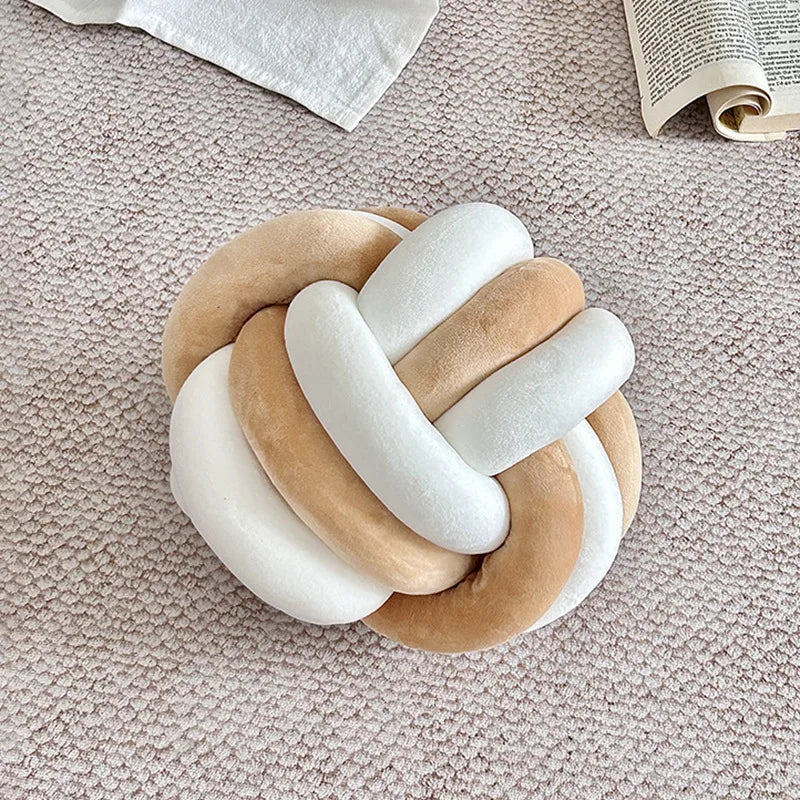 Coussin nœud bicolore blanc et camel posé sur un canapé beige