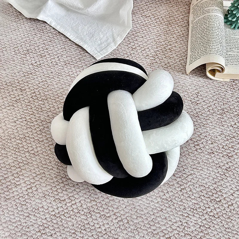 Coussin nœud bicolore en velours noir et blanc posé sur un canapé beige