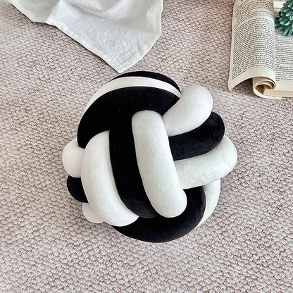 Coussin nœud bicolore en velours noir et blanc posé sur un canapé beige