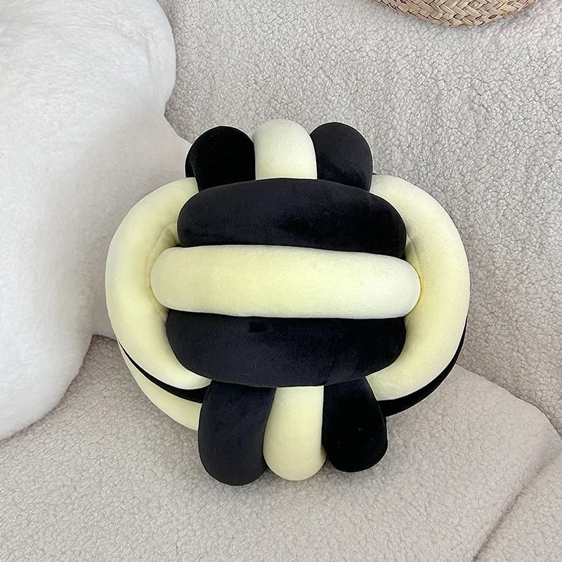 Coussin nœud bicolore en velours noir et jaune pâle sur un canapé clair