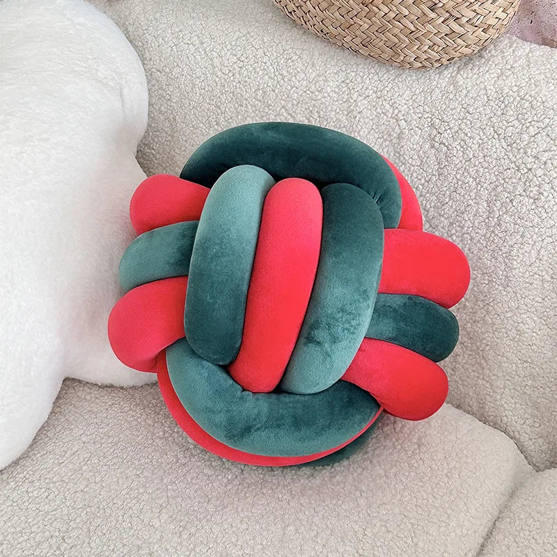 Coussin nœud bicolore en velours rouge et vert foncé sur un canapé clair