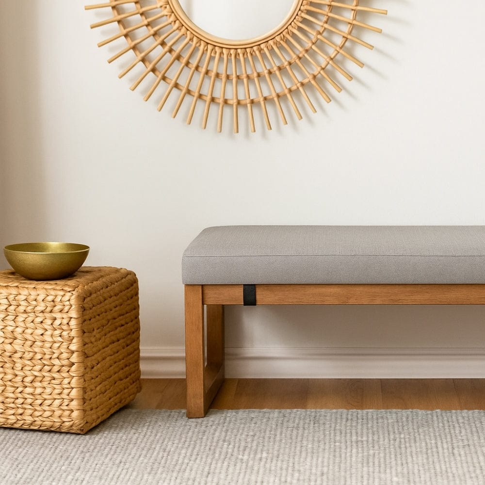 Coussin de banquette gris en tissu, posé sur un banc en bois, à côté d'un meuble en osier et d'un