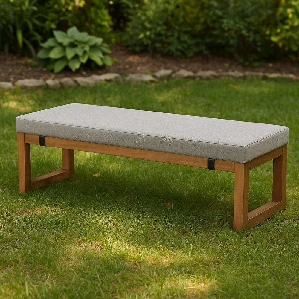 Coussin décoratif gris sur une banquette en bois, posé sur une pelouse verte entourée de plantes