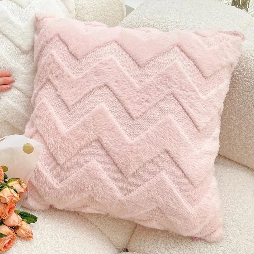 Coussin décoratif rose en tissu doux avec motif chevron, posé sur un canapé blanc et entouré de fleurs
