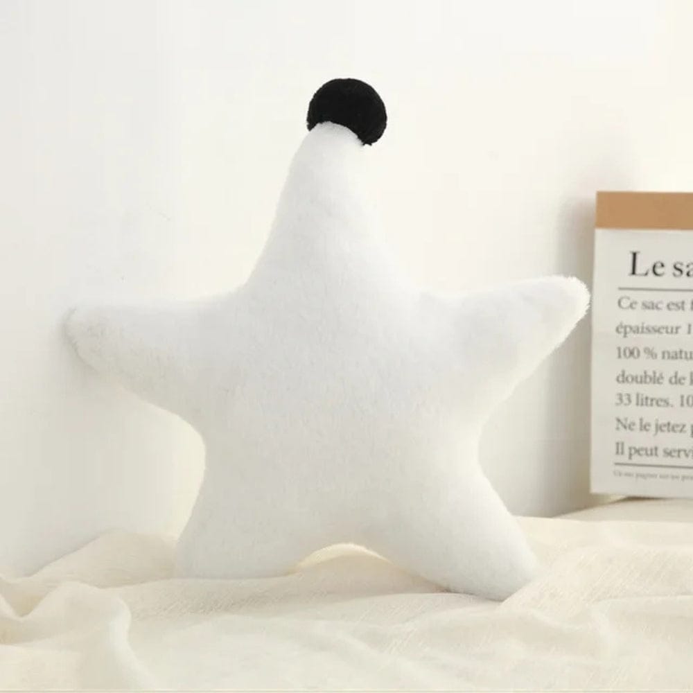 Coussin décoratif en forme d'étoile, blanc avec un pompon noir, posé sur un tissu doux dans un salon