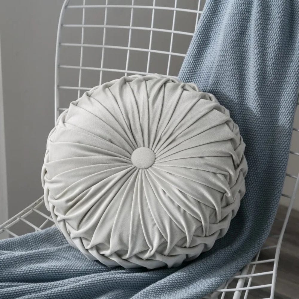 Coussin décoratif rond en velours gris clair, posé sur une chaise avec un plaid bleu
