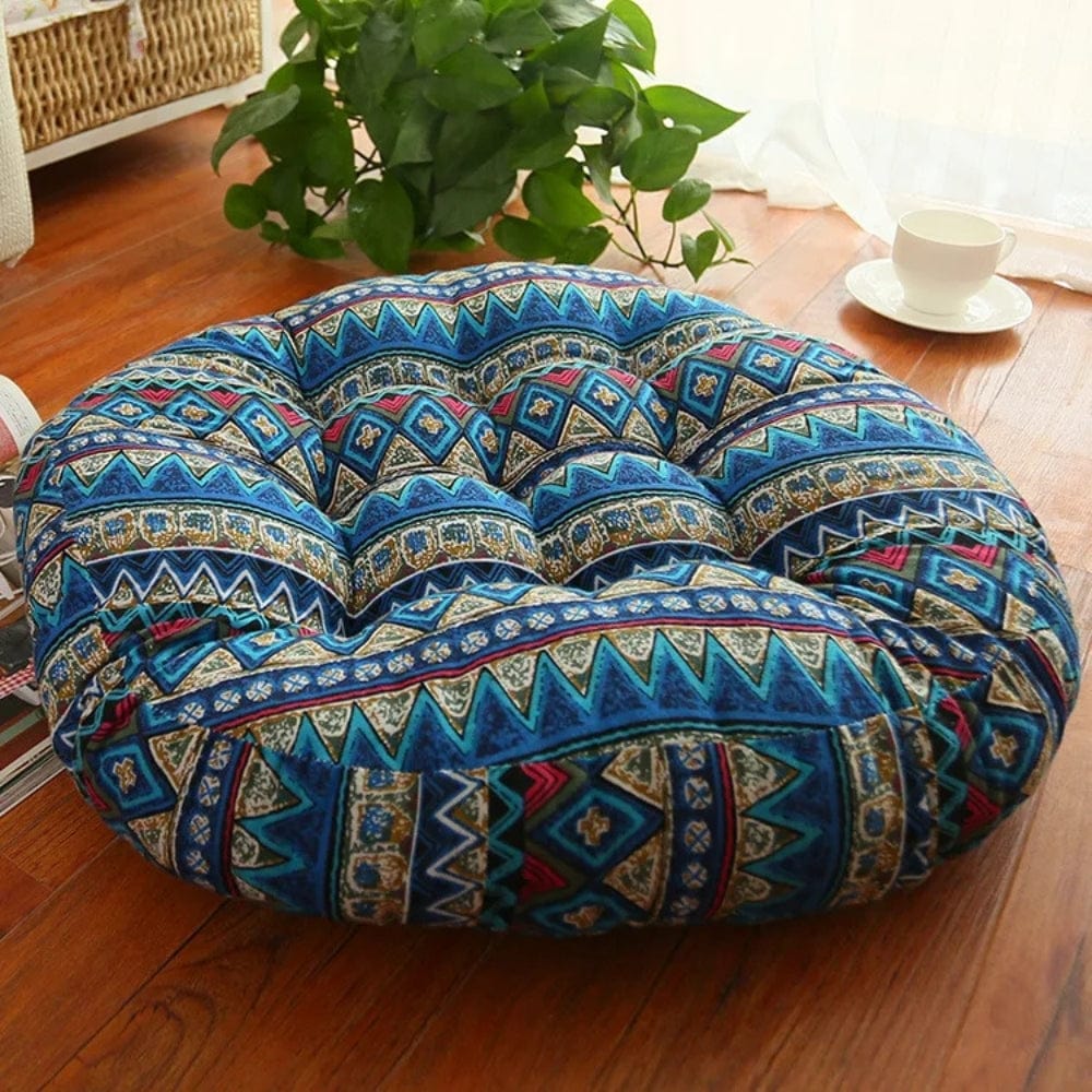 Coussin décoratif rond en tissu bleu avec motifs géométriques, posé sur un sol en bois près d'une plante
