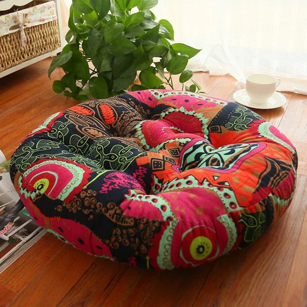 Coussin décoratif rond aux motifs bohèmes colorés, posé sur un sol en bois, entouré de verdure