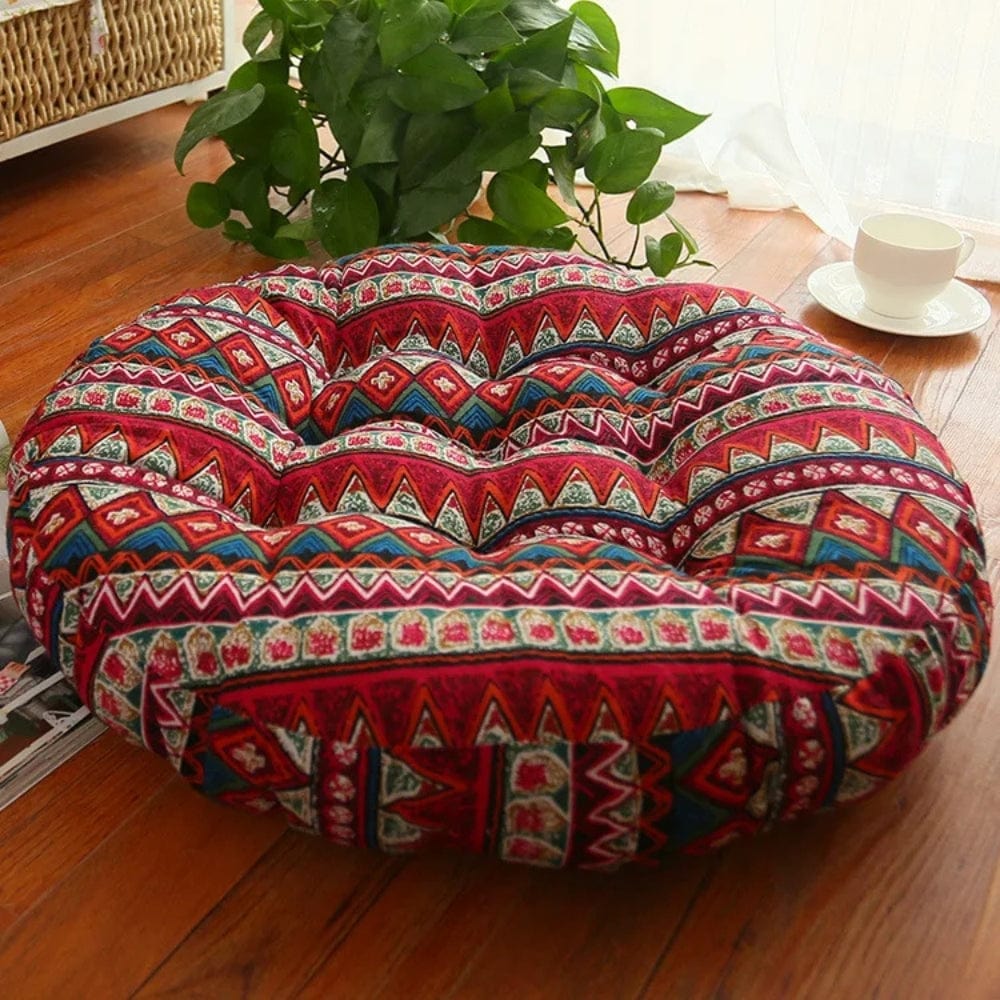 Coussin décoratif rond aux motifs colorés bohémiens, posé sur un sol en bois, à côté d'une plante verte