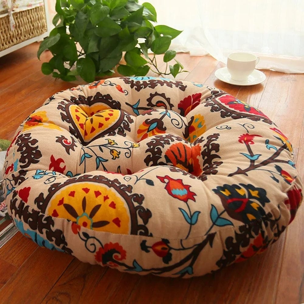 Coussin décoratif rond aux motifs bohèmes colorés, posé sur un sol en bois, près d'une plante verte