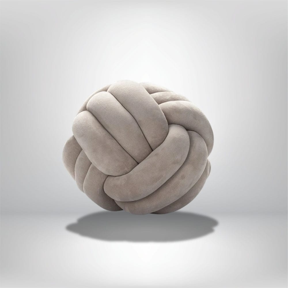Coussin décoratif en forme de boule nouée, en velours doux de couleur beige, posé sur un fond neutre