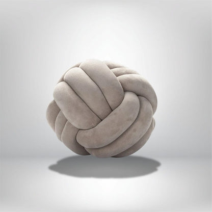 Coussin décoratif en forme de boule nouée, en velours doux de couleur beige, posé sur un fond neutre