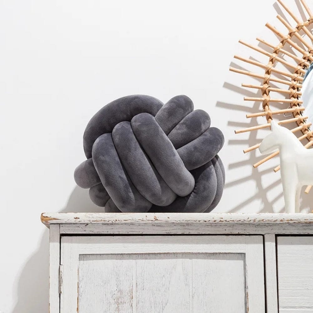 Coussin décoratif en forme de noeud, en velours gris, posé sur un meuble en bois blanc