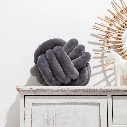 Coussin décoratif en forme de noeud, en velours gris, posé sur un meuble en bois blanc