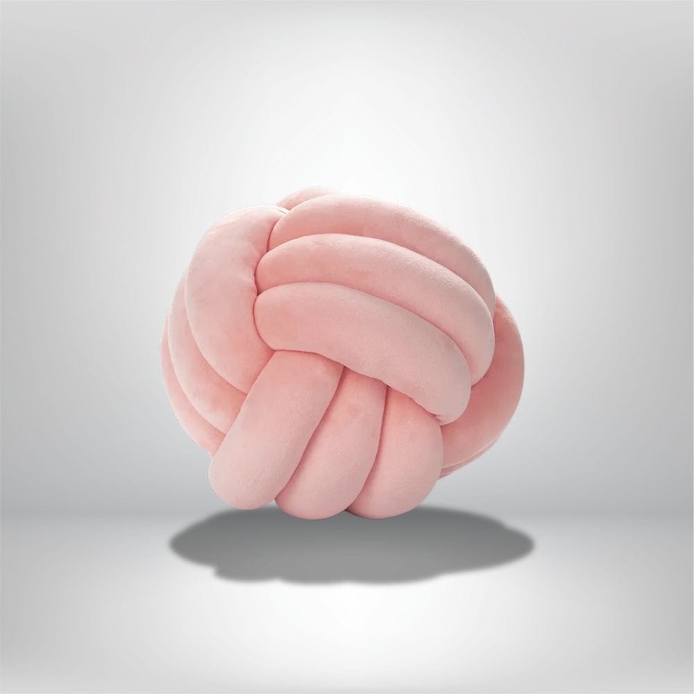 Coussin décoratif en forme de boule nouée, en velours rose, posé sur un fond neutre