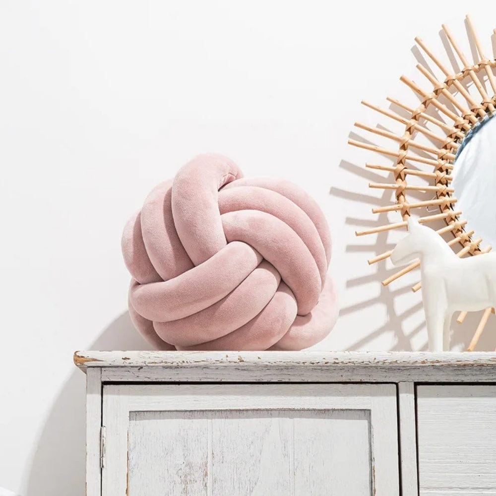 Coussin décoratif en velours rose en forme de nœud, posé sur un meuble en bois blanc