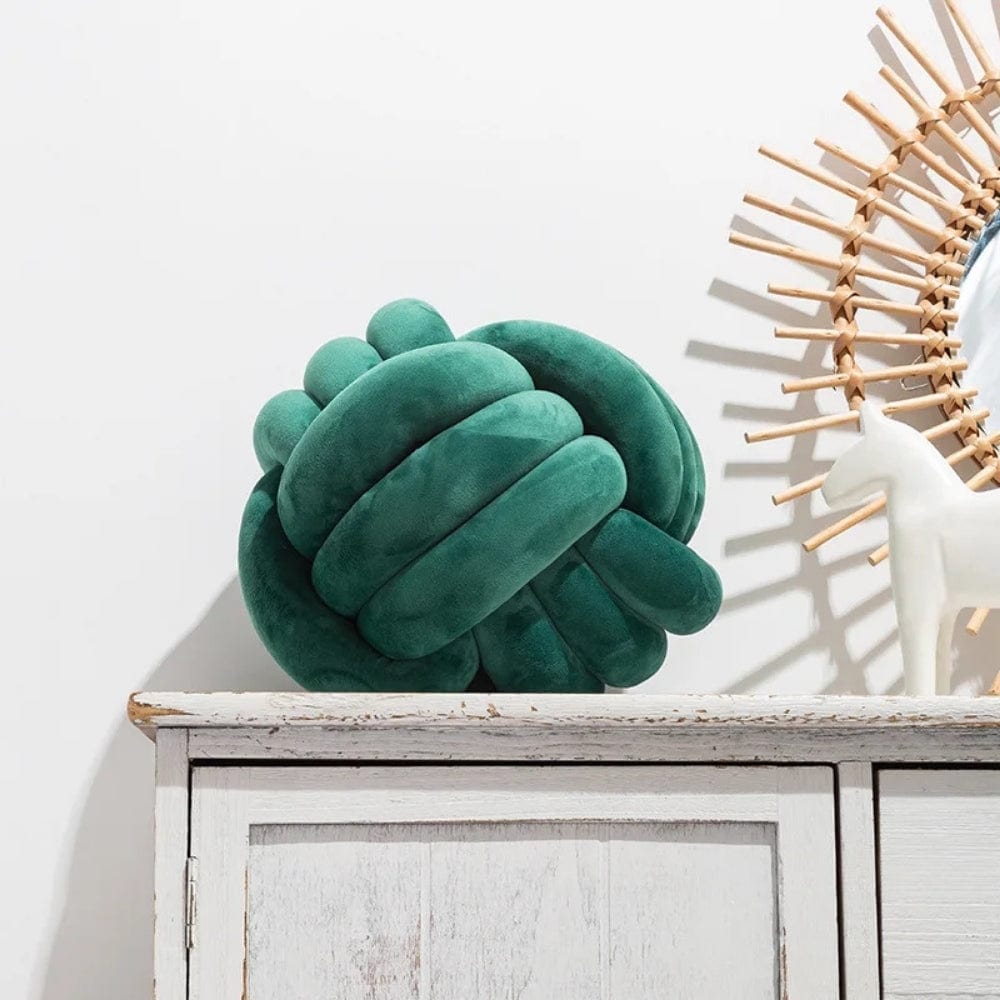 Coussin décoratif en velours vert en forme de boule noeud, posé sur un meuble en bois blanc