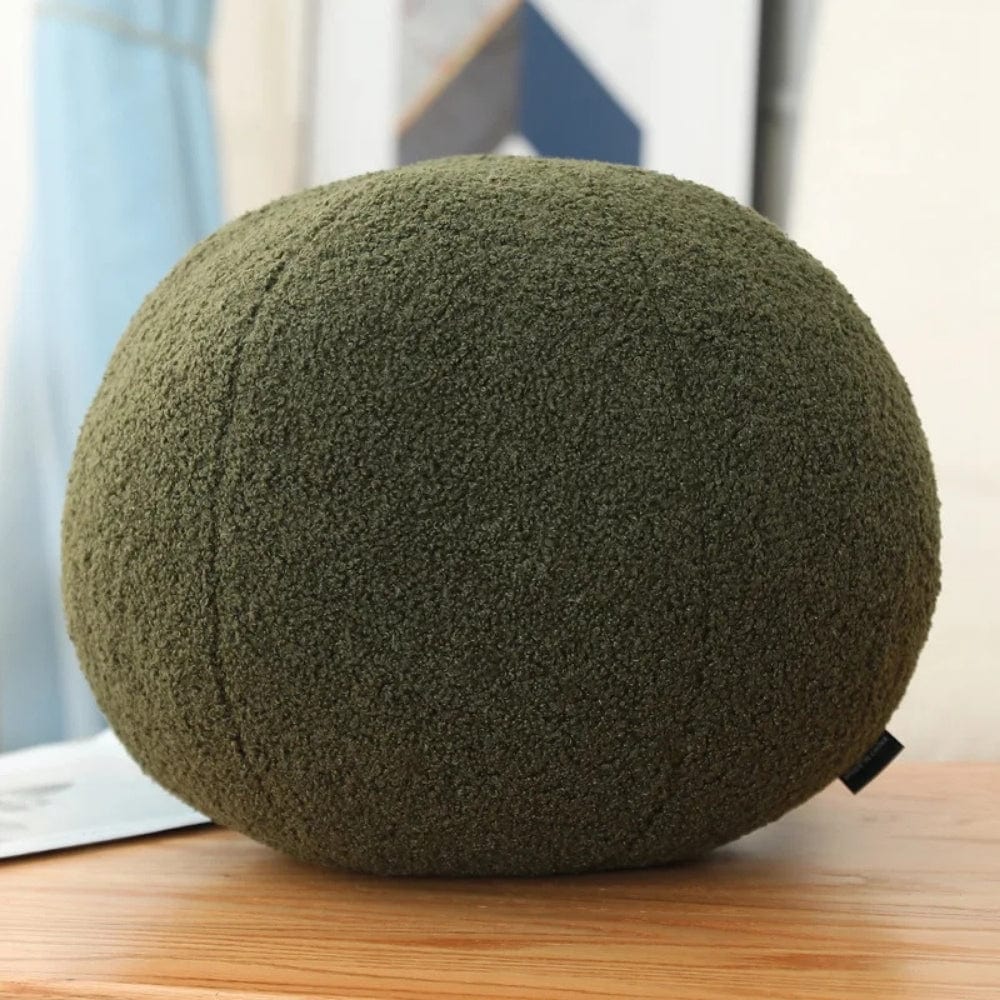 Coussin boule en velours vert olive posé sur une table en bois, ajoutant une touche décorative à un intérieur moderne