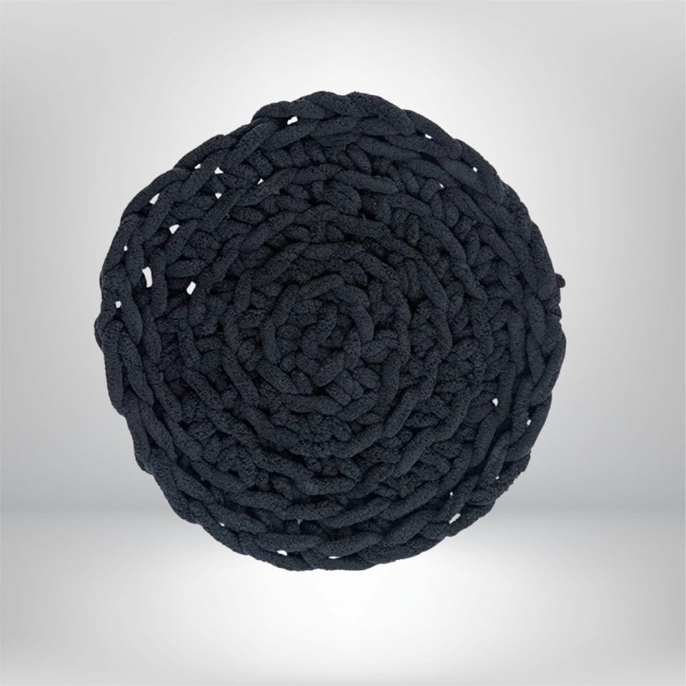 Coussin déco rond en tissu noir, tressé avec un motif spiral, posé sur un fond neutre