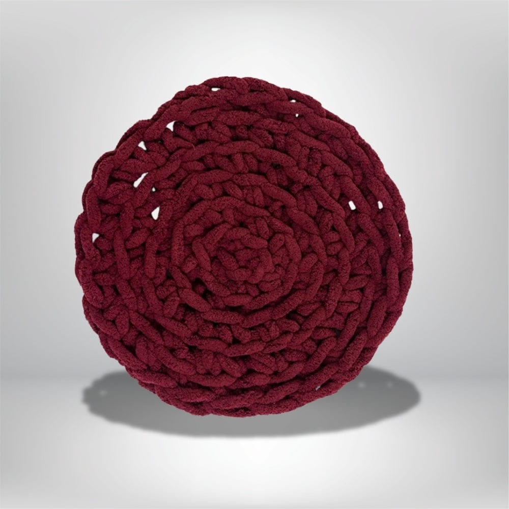 Coussin déco rond en tissu bordeaux, tressé en spirale, posé sur une surface neutre, idéal pour un salon moderne