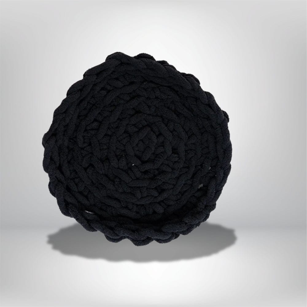 Coussin déco noir en tissu tressé, de forme ronde, posé sur une surface neutre