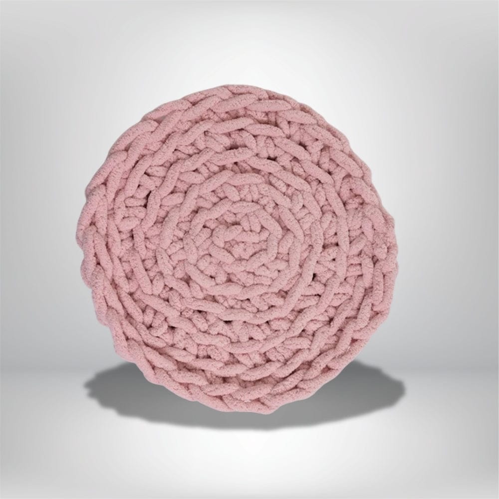 Coussin décoratif rond en tissu rose, avec un motif tressé, posé sur une surface neutre