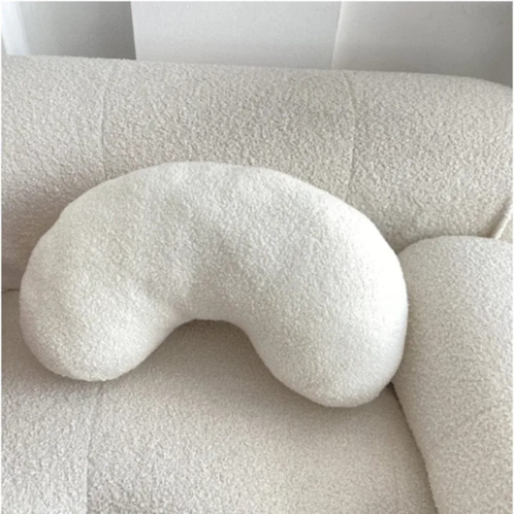 Coussin décoratif blanc en forme de haricot sur un canapé beige texturé dans un salon moderne