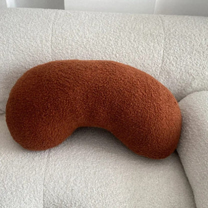 Coussin décoratif en forme de haricot, en tissu doux couleur terracotta, posé sur un canapé clair