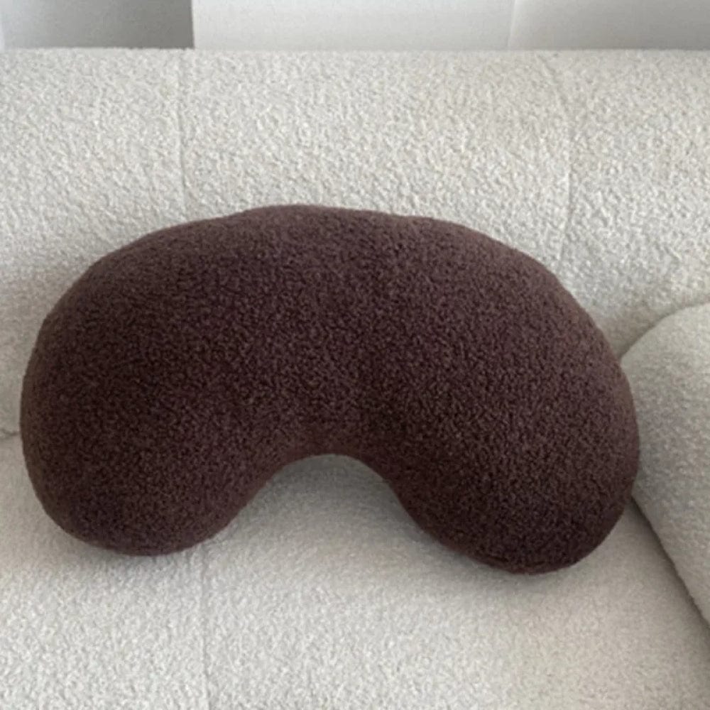 Coussin déco en forme de haricot, couleur marron, posé sur un canapé beige texturé