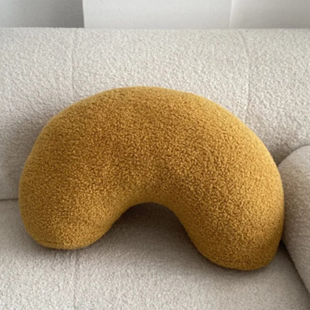 Coussin décoratif en forme de haricot, couleur jaune moutarde, posé sur un canapé beige texturé