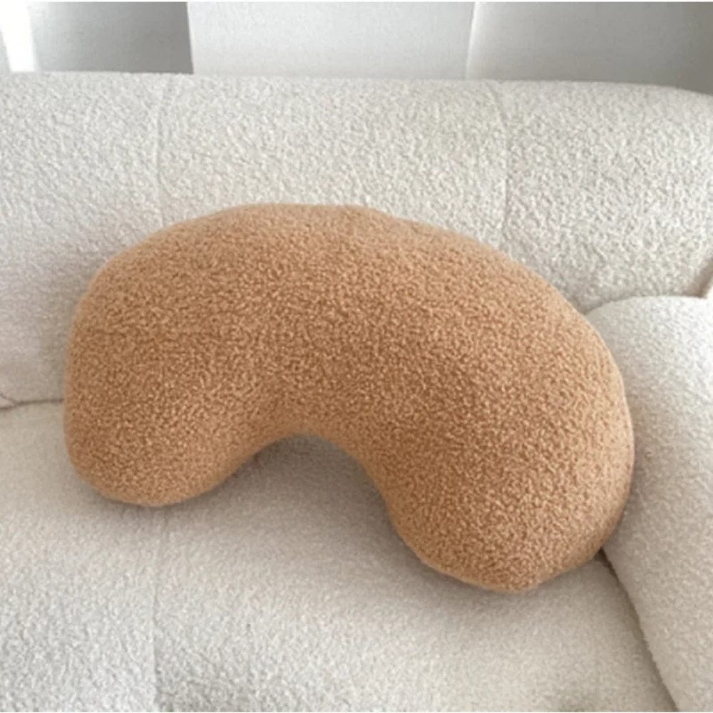 Coussin décoratif en forme de haricot, couleur beige, en matière douce sur un canapé blanc