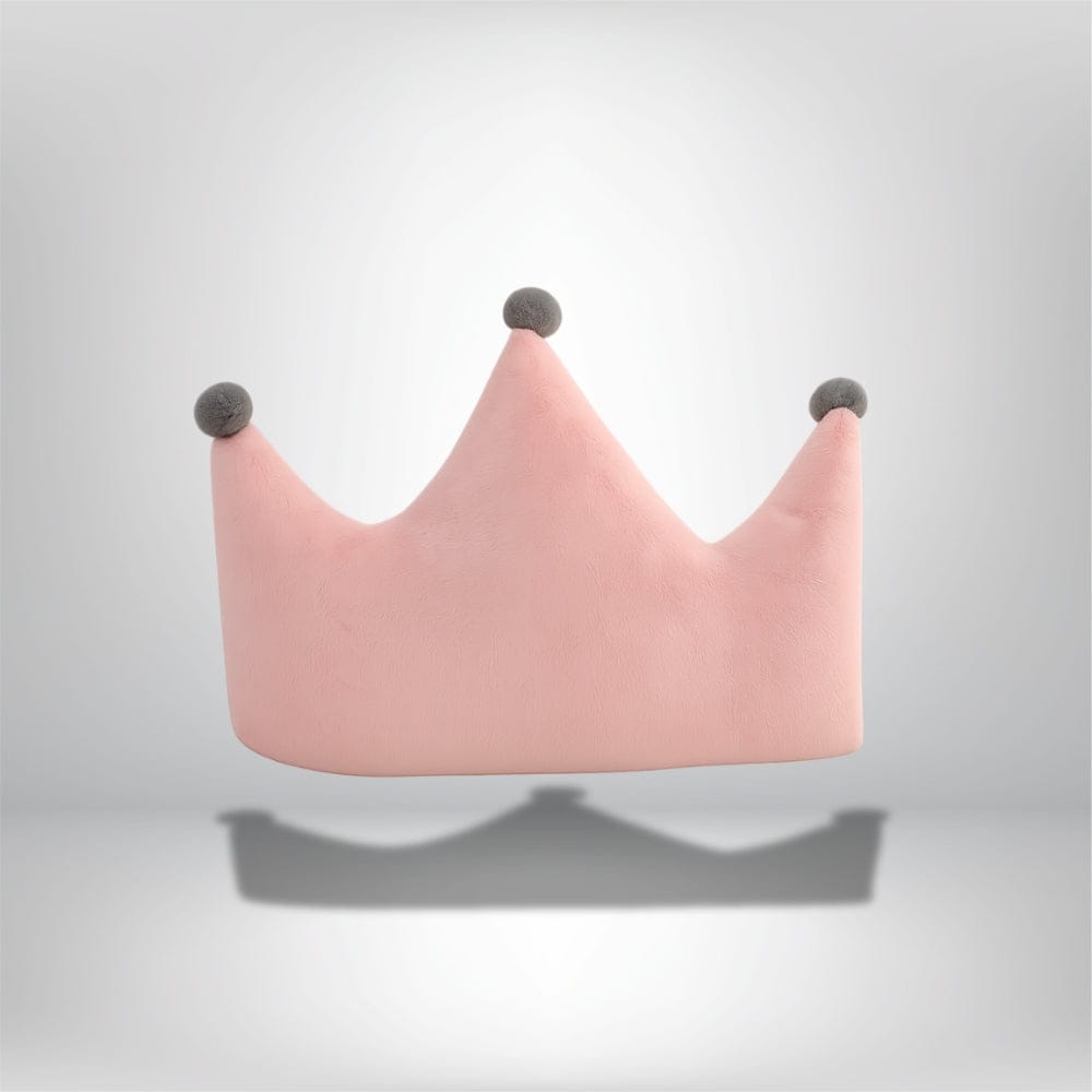 Coussin déco rose en forme de couronne avec pompons gris, posé sur une surface neutre