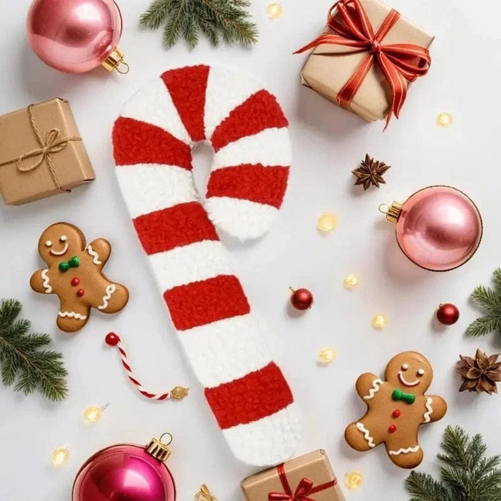 Coussin décoratif en forme de canne à sucre rouge et blanc, posé sur une table de Noël avec des décorations