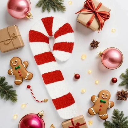 Coussin décoratif en forme de canne à sucre rouge et blanc, posé sur une table de Noël avec des décorations