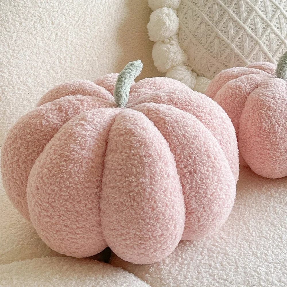 Coussin décoratif en forme de citrouille rose, en matière douce, posé sur un canapé beige