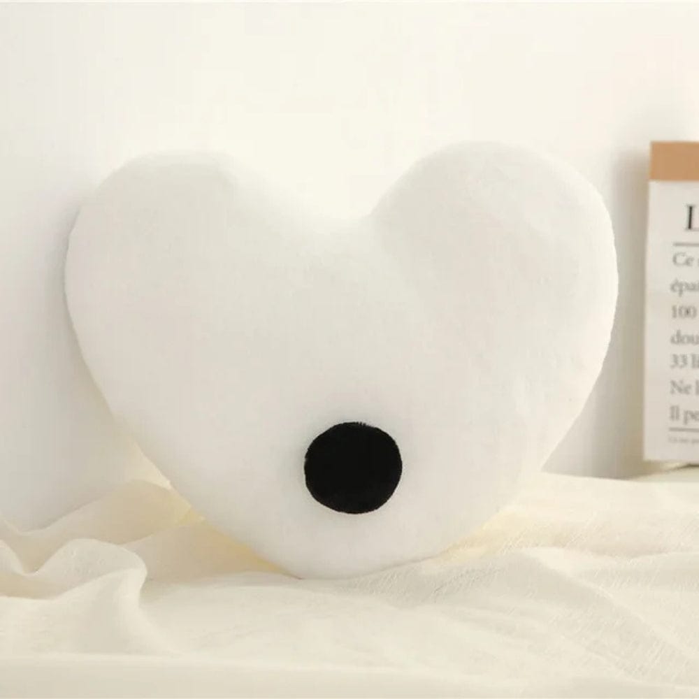Coussin décoratif en forme de cœur blanc avec un motif noir, posé sur un tissu doux dans un salon