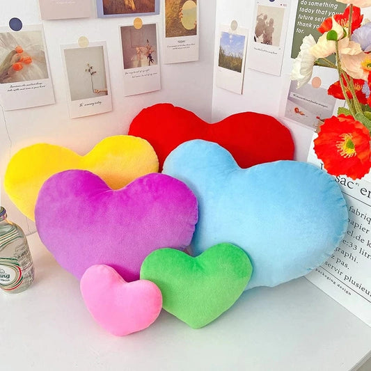 Coussins décoratifs en forme de cœur, aux couleurs vives, disposés sur une surface blanche avec des éléments de décoration