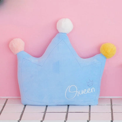 Coussin décoratif en forme de couronne, bleu avec pompons pastel, posé sur un fond rose