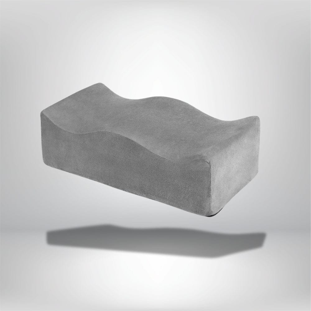 Coussin ergonomique gris en velours, à la forme ondulée, posé sur un fond neutre