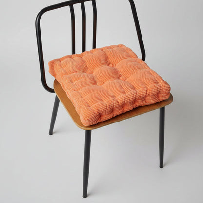 Coussin d'assise en velours côtelé orange, décoratif, posé sur un fond neutre