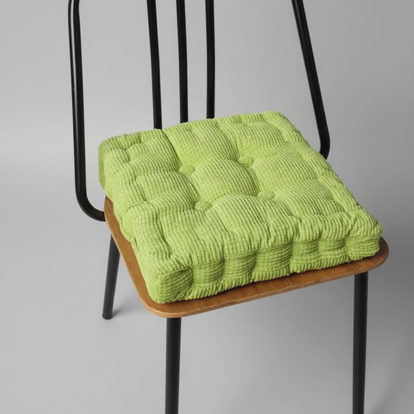 Coussin de chaise en velours côtelé vert, avec un motif matelassé, posé sur un fond neutre