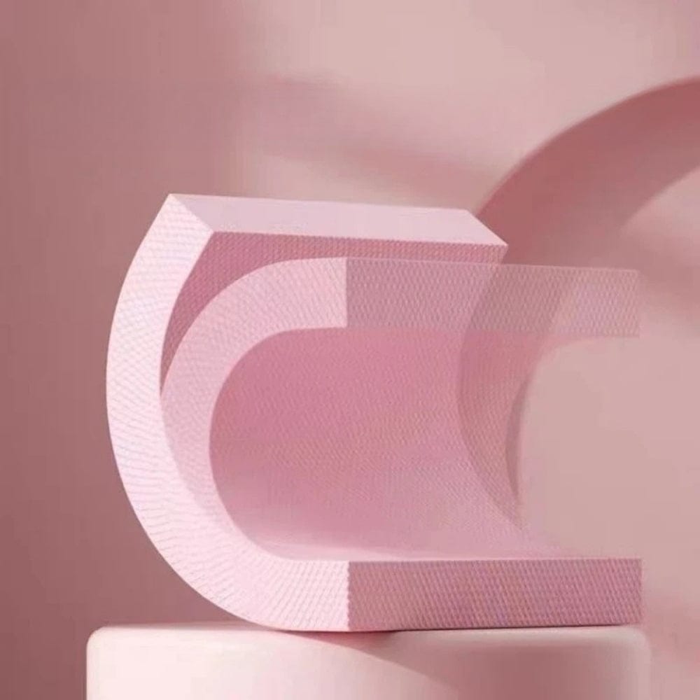 Coussin décoratif en forme de C, en matière rose texturée, posé sur une surface neutre