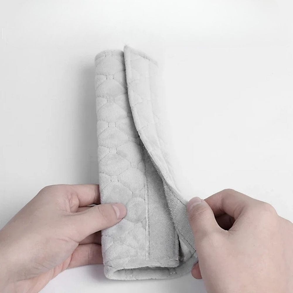 Coussin de ceinture de sécurité en tissu gris, doux et matelassé, tenu par une main sur fond blanc