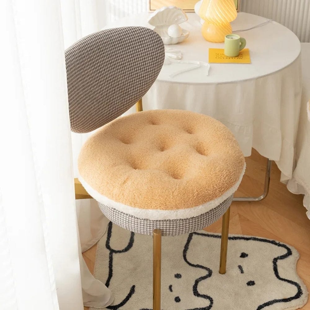 Coussin de chaise rond en tissu beige et motif à carreaux, placé sur une chaise dorée dans un salon lumineux