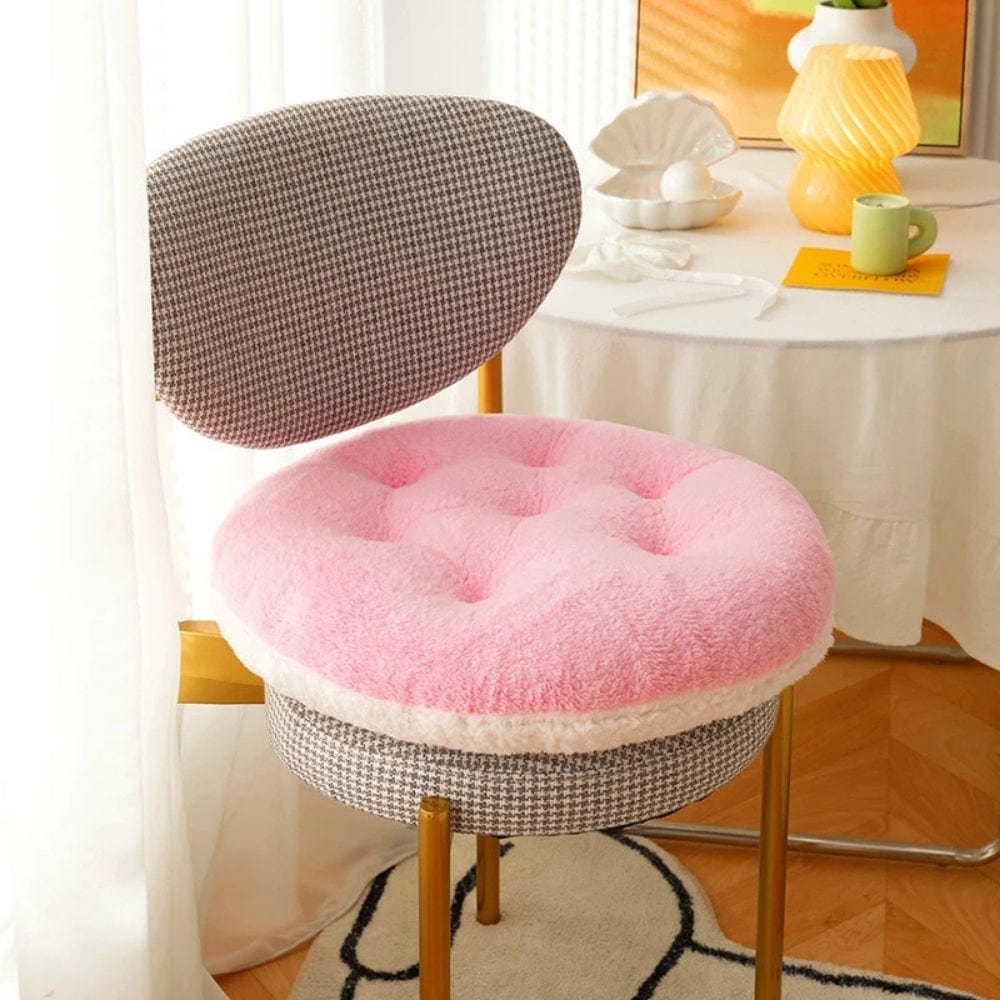 Coussin de chaise rond en velours rose, avec des boutons, sur une chaise à motifs check et un décor lumineux