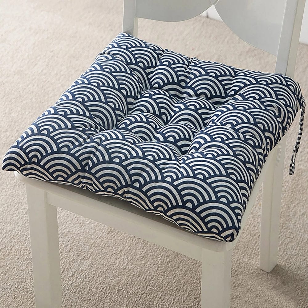 Coussin de chaise de jardin avec motif ondulé bleu et blanc, posé sur une chaise blanche dans un intérieur lumineux
