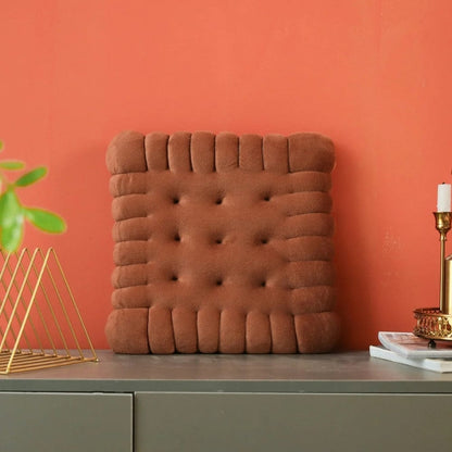 Coussin de chaise design en velours marron avec des boutons, posé sur un meuble gris devant un mur orange