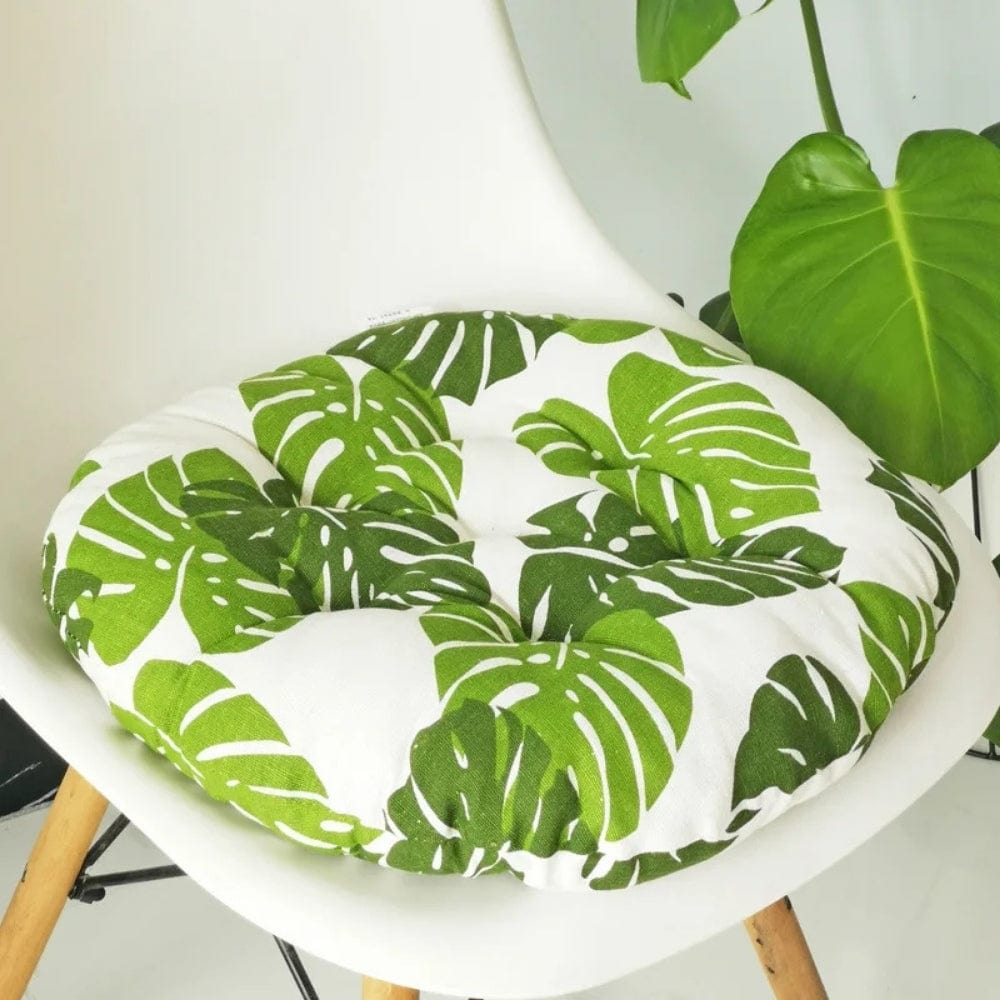 Coussin de chaise rond avec motifs de feuilles vertes sur fond blanc, posé sur une chaise moderne