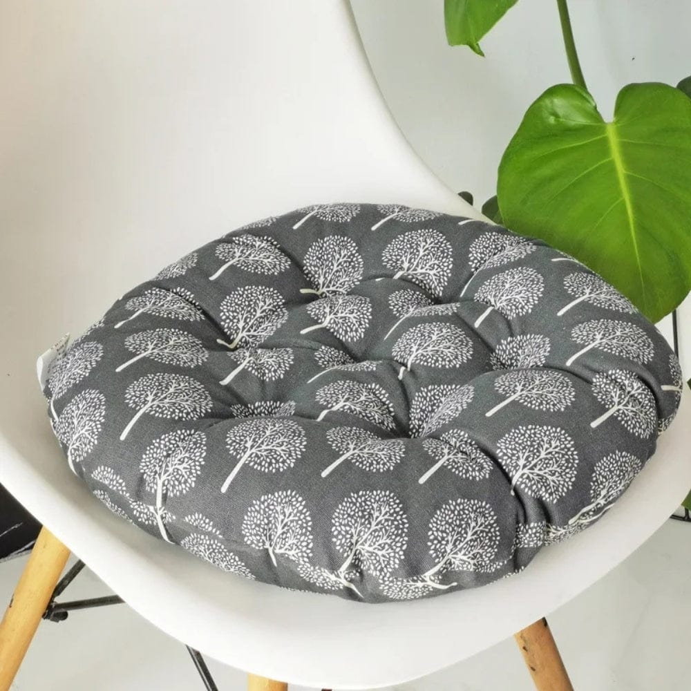 Coussin de chaise rond en tissu gris avec motifs d'arbres blancs, posé sur une chaise moderne